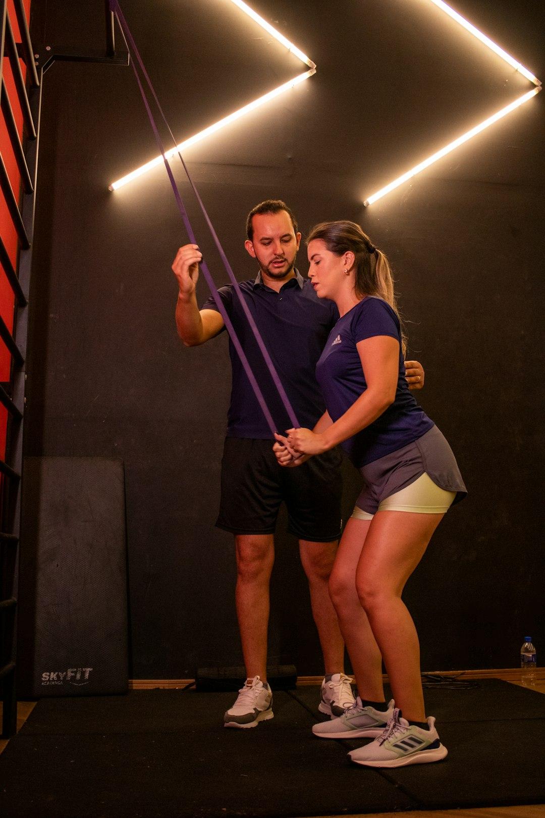 A physical therapist supervising a middle-aged adult doing a resistance-band exercise indoors and correcting their form