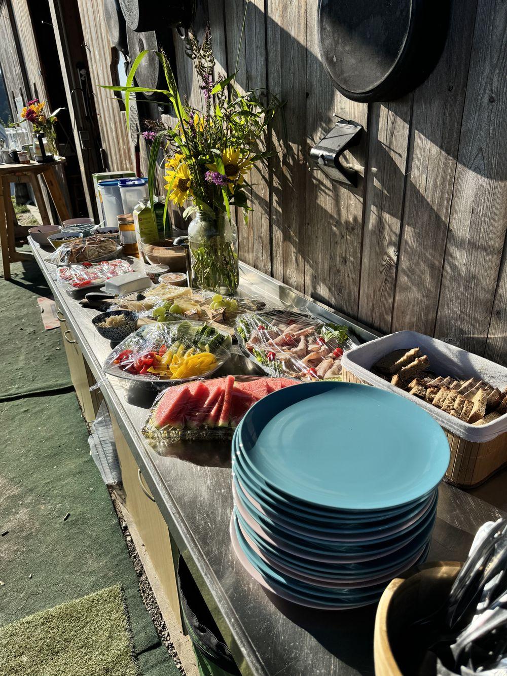 Buffet im Freien mit frischen regionalen Speisen, Gemüse, Broten und Sonnenblumen vor einer Holzwand