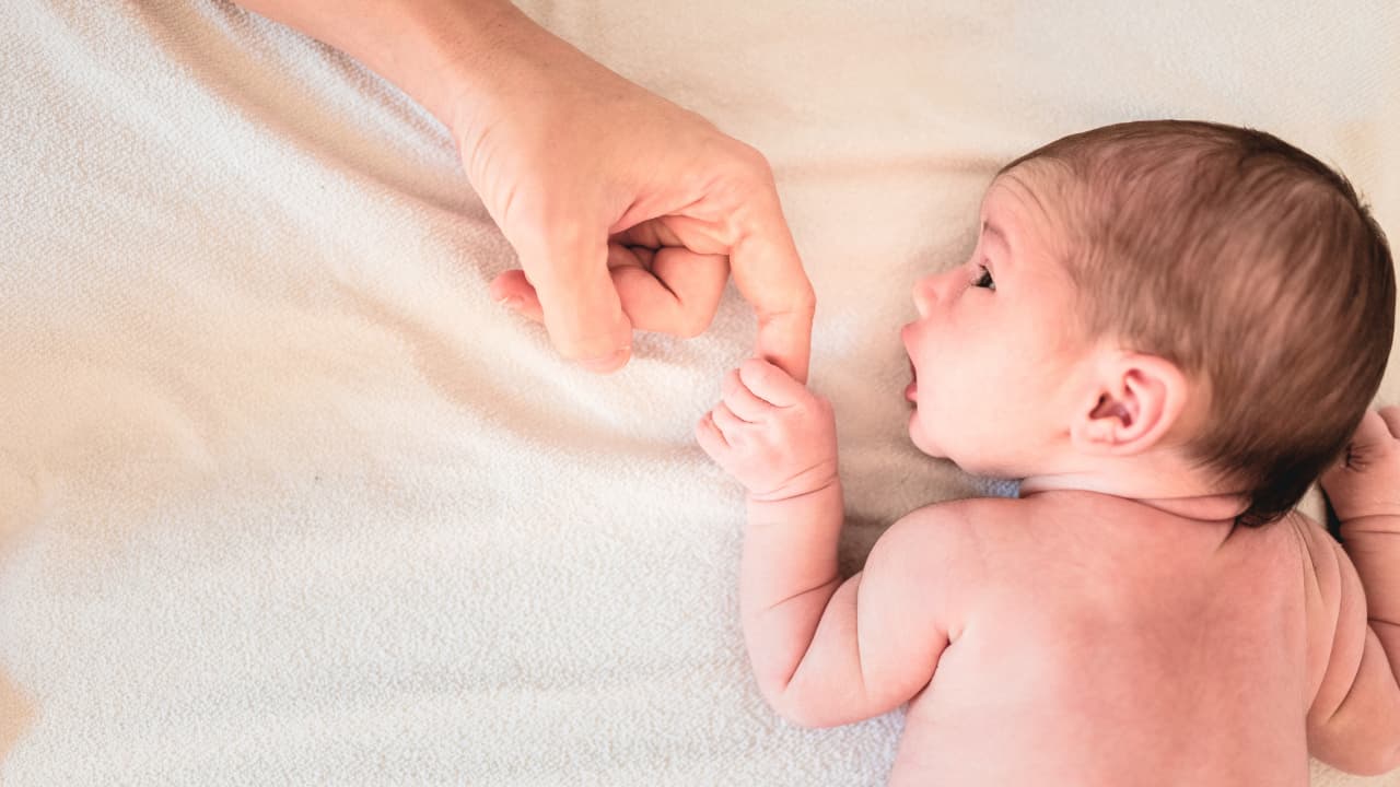 Newborn baby holding a parent's finger while lying on a bed