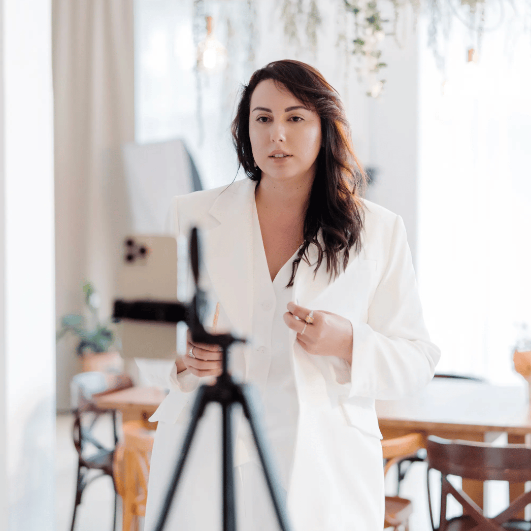 Woman recording a video for her marketing standing in front of a tripod that's holding her iphone.