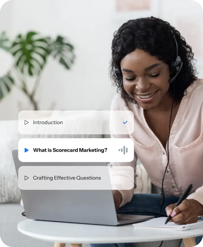 Woman wearing a headset takes notes while watching a 'What is Scorecard Marketing?' video mini-course lesson on her laptop