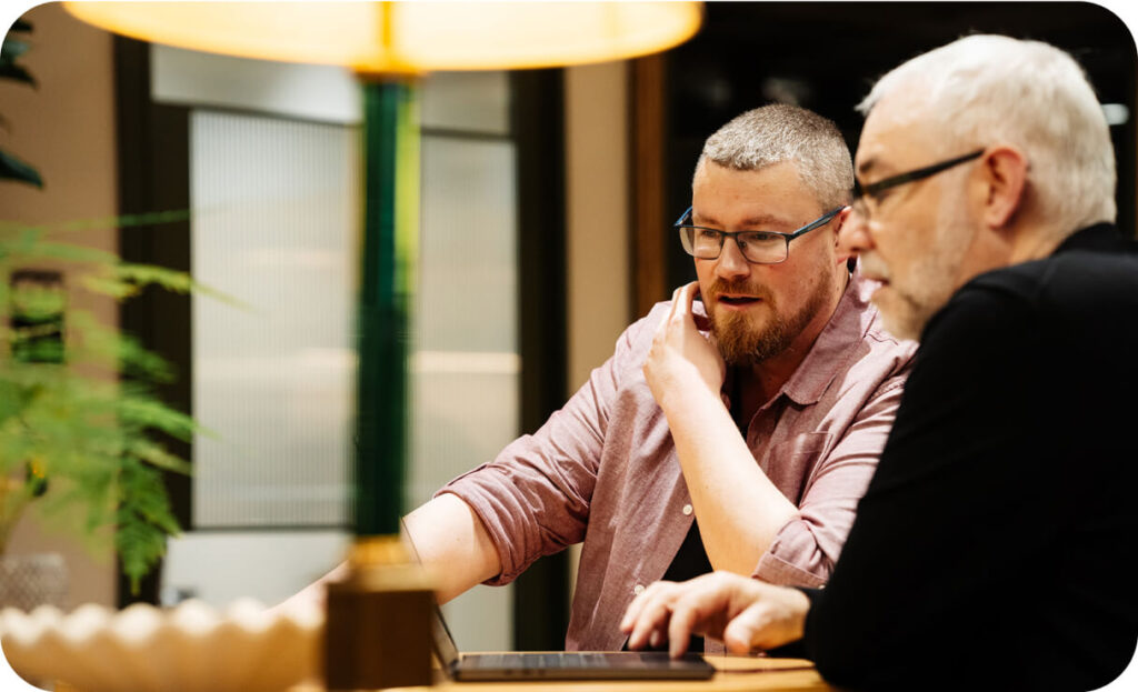Two colleagues reviewing work together on a tablet at a desk in a modern office setting.