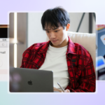 Young man in a red flannel shirt working on a MacBook, with Gmail open in Safari and a phone showing 6,753 unread emails nearby.