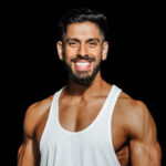 Akash, a fitness coach, smiling and wearing a white tank top against a dark background.