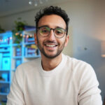 Smiling man with glasses and a white sweater in a modern office setting