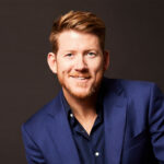 Glen, a smiling man with red hair and beard wearing a navy blazer, professional headshot