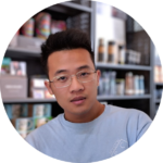 Person wearing glasses and a light blue Houston shirt, seated in front of shelves with products