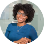 Smiling woman wearing glasses and a blue top, with arms folded, in a professional office setting.